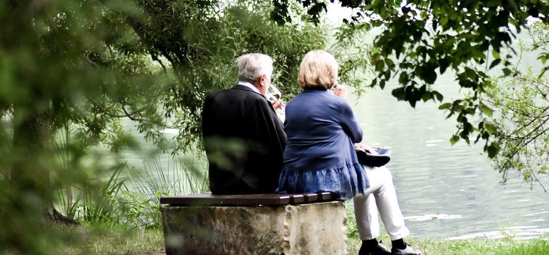 image1 two elderly people drinking wine sitting on a bench next to a river